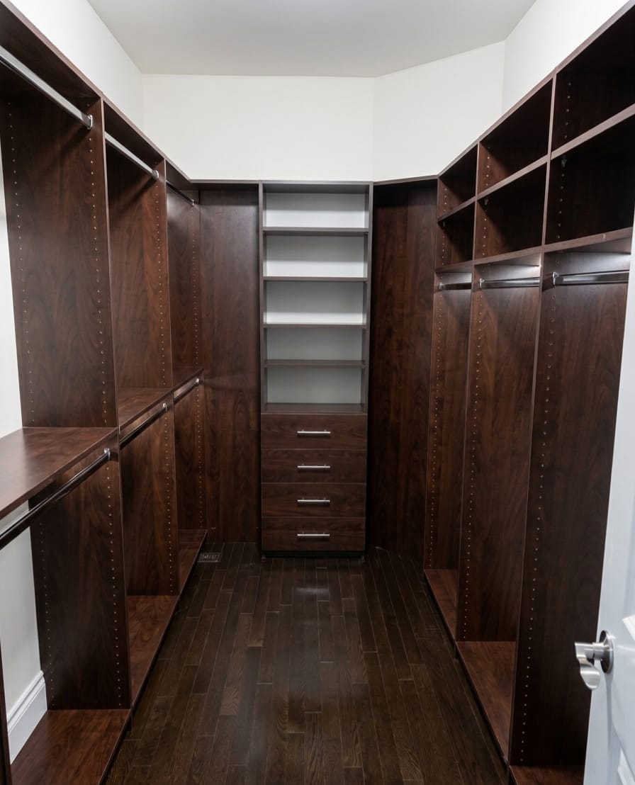 Finished Oakville walk-in closet with dark walnut custom millwork, double hanging sections, open cubbies, and central drawer tower
