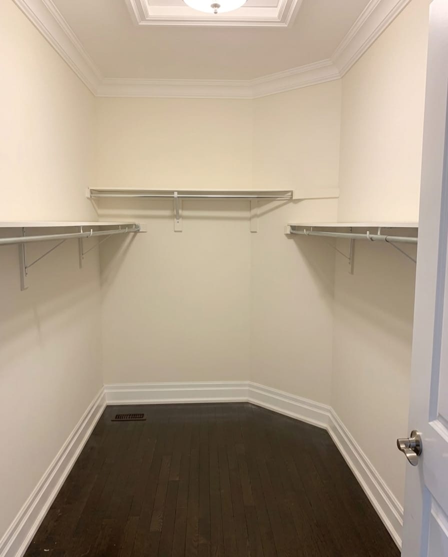 Basic walk-in closet in Oakville with single hanging rods and empty walls before custom cabinetry installation